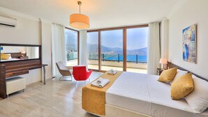 A hotel room with a large bed, a desk, a chair, and a view of the sea.