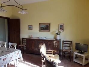 A dining area with a wooden cabinet, a TV on a stand, and a table with chairs. - Agriturismo Il Pescinone - Oleandro, between the countryside and the sea (Pescinone)