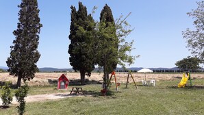 A park with picnic tables, a red playhouse, and a yellow slide.