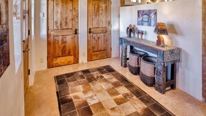 Un couloir avec des portes en bois, un tapis à motifs, une console ornée d’objets décoratifs et un miroir au mur.