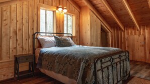 Een slaapkamer in een houten chalet, met een bed, nachtkastje en raam.