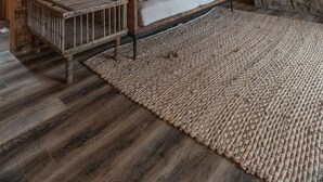 Een rustiek cabin interieur met een houten plafond, een stenen open haard, een bank met kussens en een lijst met een afbeelding van een hert op de muur.