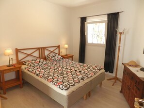 Ein Schlafzimmer mit einem Bett, zwei Nachttischen, einer Kommode und einem Fenster mit Vorhängen.