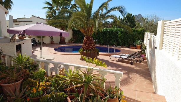 A pool area with a palm tree, lounge chairs, and a purple umbrella. - Casa Zinat para 4 Personas (Calpe)