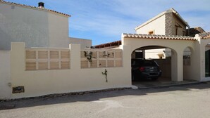 A gated entrance with a car parked inside, a stone building with a tiled roof, and a clear sky. - Casa Zinat para 4 Personas (Calpe)