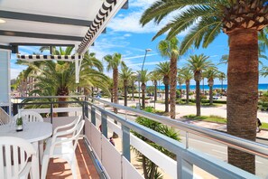 A balcony with a white table and chairs, overlooking a palm tree-lined street and beach. - Fantastic Sea Front Apartment - UHC RODAS 322 (Salou)