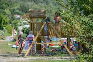 A wooden play structure with multiple levels and a slide, surrounded by grassy area and trees. - Directly on the lake with panoramic views (Tre Capitelli)