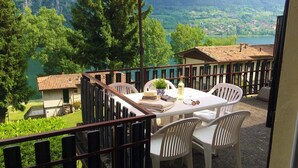 A balcony with a table and chairs, a red umbrella, and a scenic view of a lake and mountains. - Directly on the lake with terrace and two bedrooms (Idro)