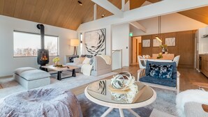 A spacious living room with a fireplace, a sofa, a coffee table, and a dining area with chairs. - Koa Niseko (Niseko)