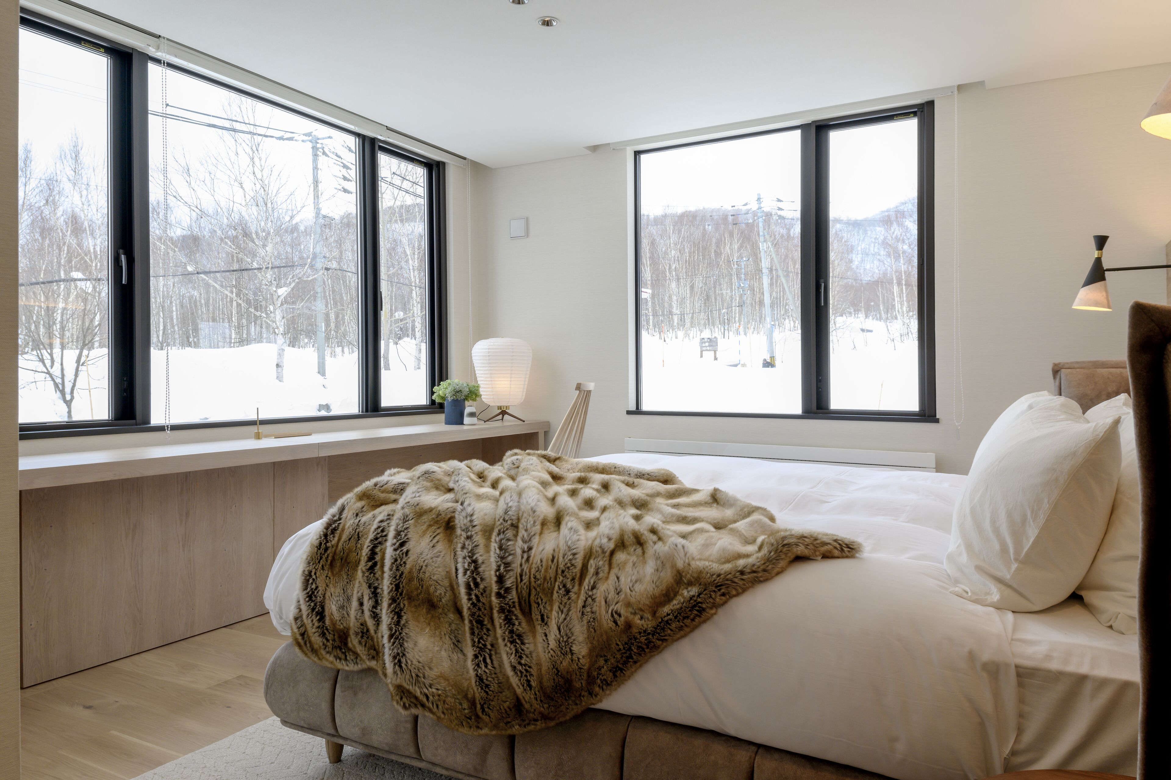A bedroom with a large bed, a window seat, and a view of a snowy landscape.