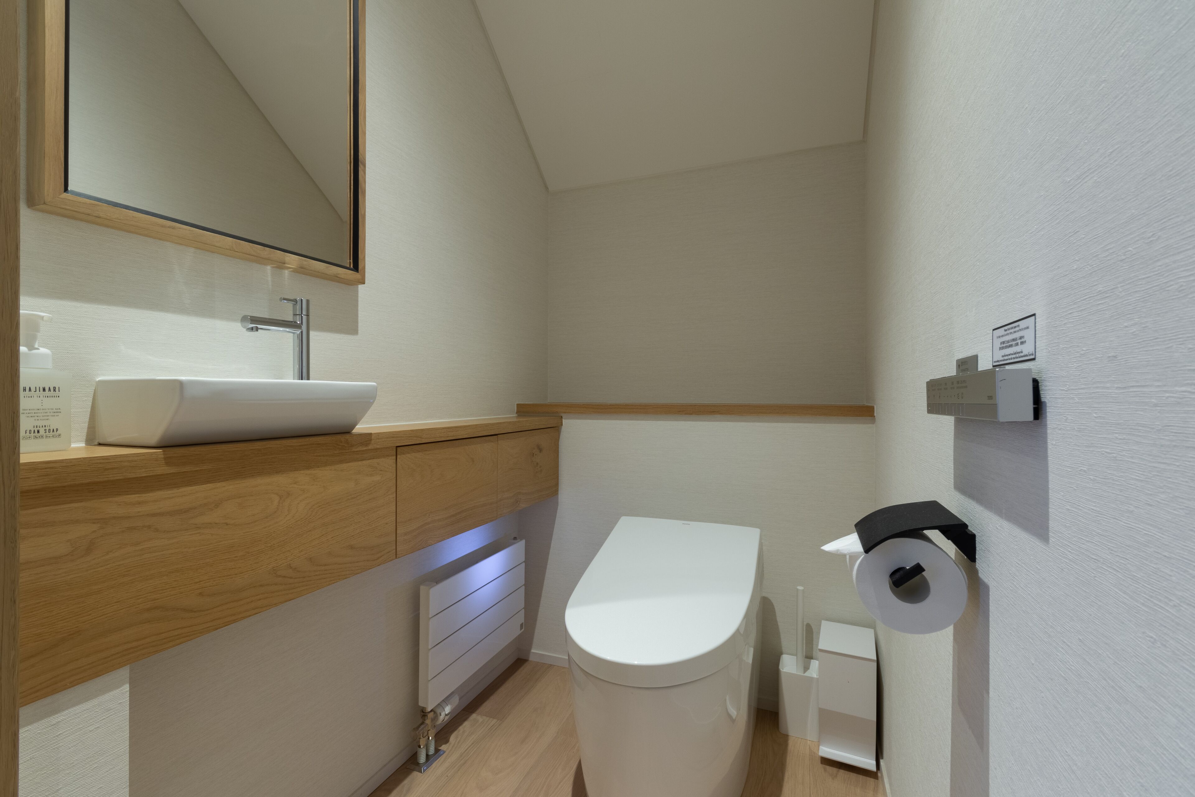 Un bagno moderno con un mobile lavabo in legno, un lavabo bianco, un water e un portasciugamani a muro.
