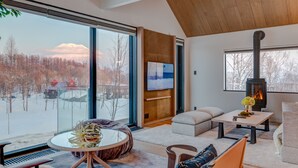A modern living room with a large window, a fireplace, and a cozy seating area. - Koa Niseko (Niseko)