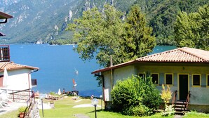 A coastal building with a tiled roof, surrounded by lush greenery and a view of the sea. - Directly on the lake with terrace and two bedrooms (Idro)