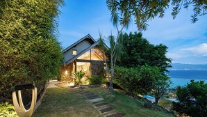 A house with a stone facade, a stone pathway leading to the entrance, and a view of the ocean. - Beautiful architect villa overlooking the lagoon and the island of Tahiti (Te'avaro)