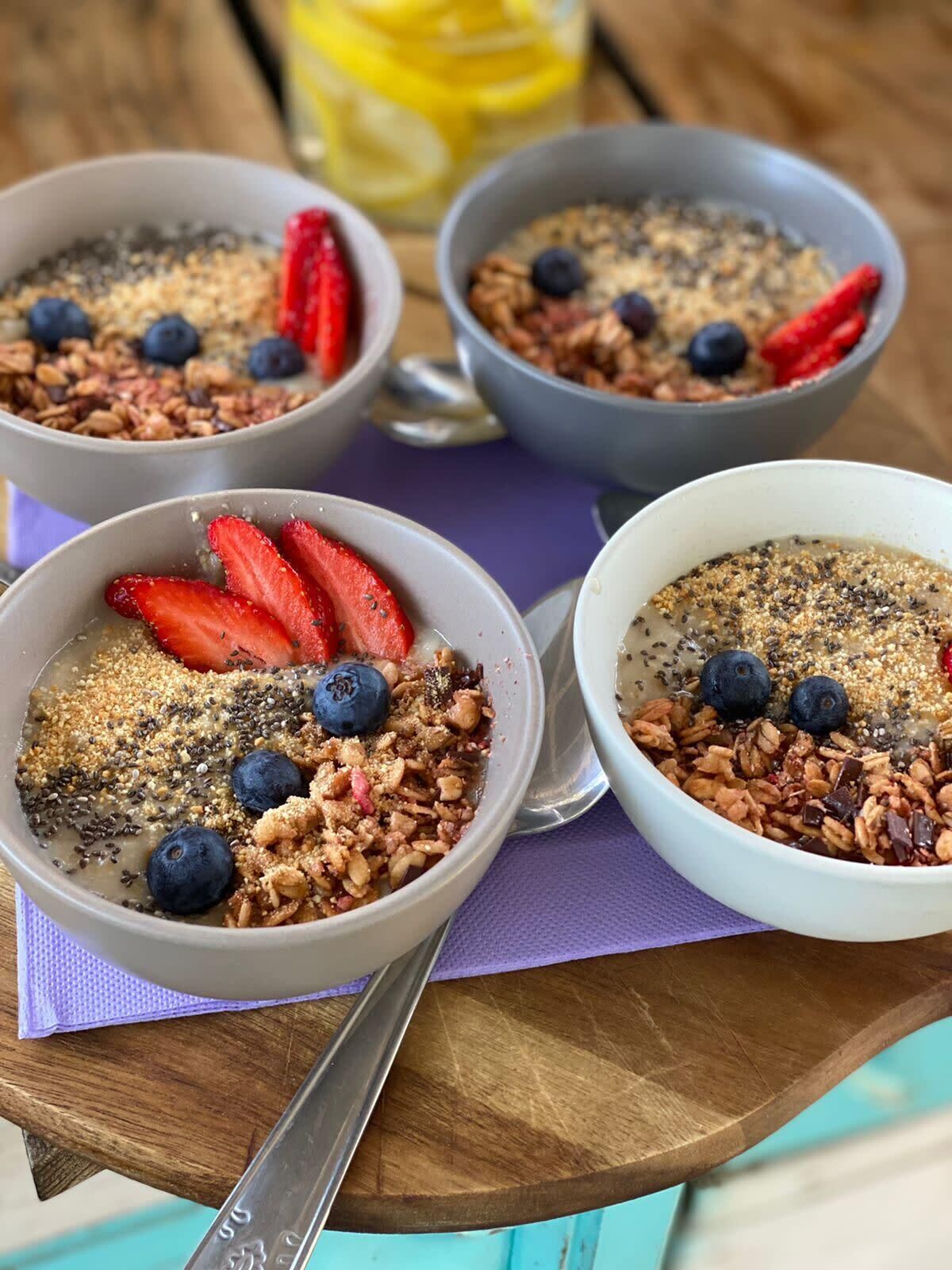 Three bowls of oatmeal with strawberries and blueberries on a wooden table.
