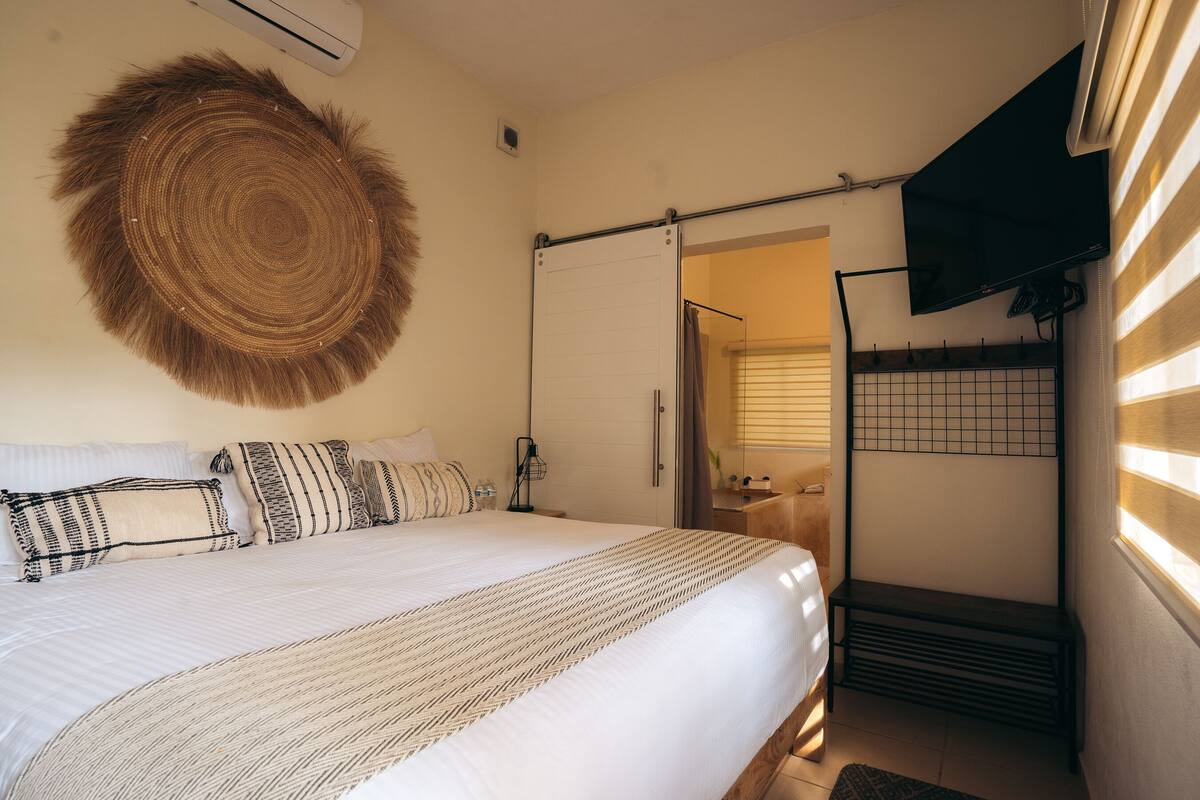Une chambre à coucher bien aménagée, avec un grand lit, un téléviseur fixé au mur et un climatiseur mural.