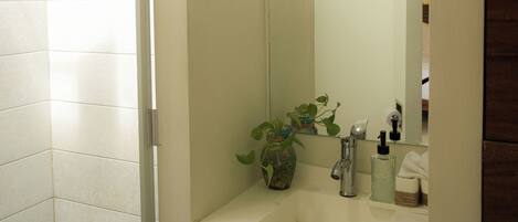 A bathroom with a white sink, a mirror, a potted plant, and a shower area.
