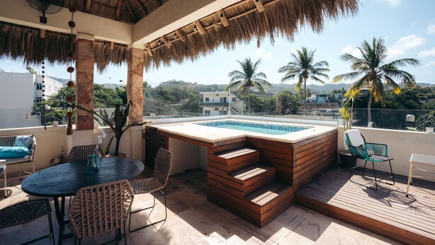 A rooftop pool area with wooden deck, seating, and a thatched roof. - Nuiya Hoteles (Sayulita)