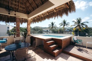 Un espace piscine sur le toit, doté d’une terrasse en bois, de sièges et d’un toit en chaume.
