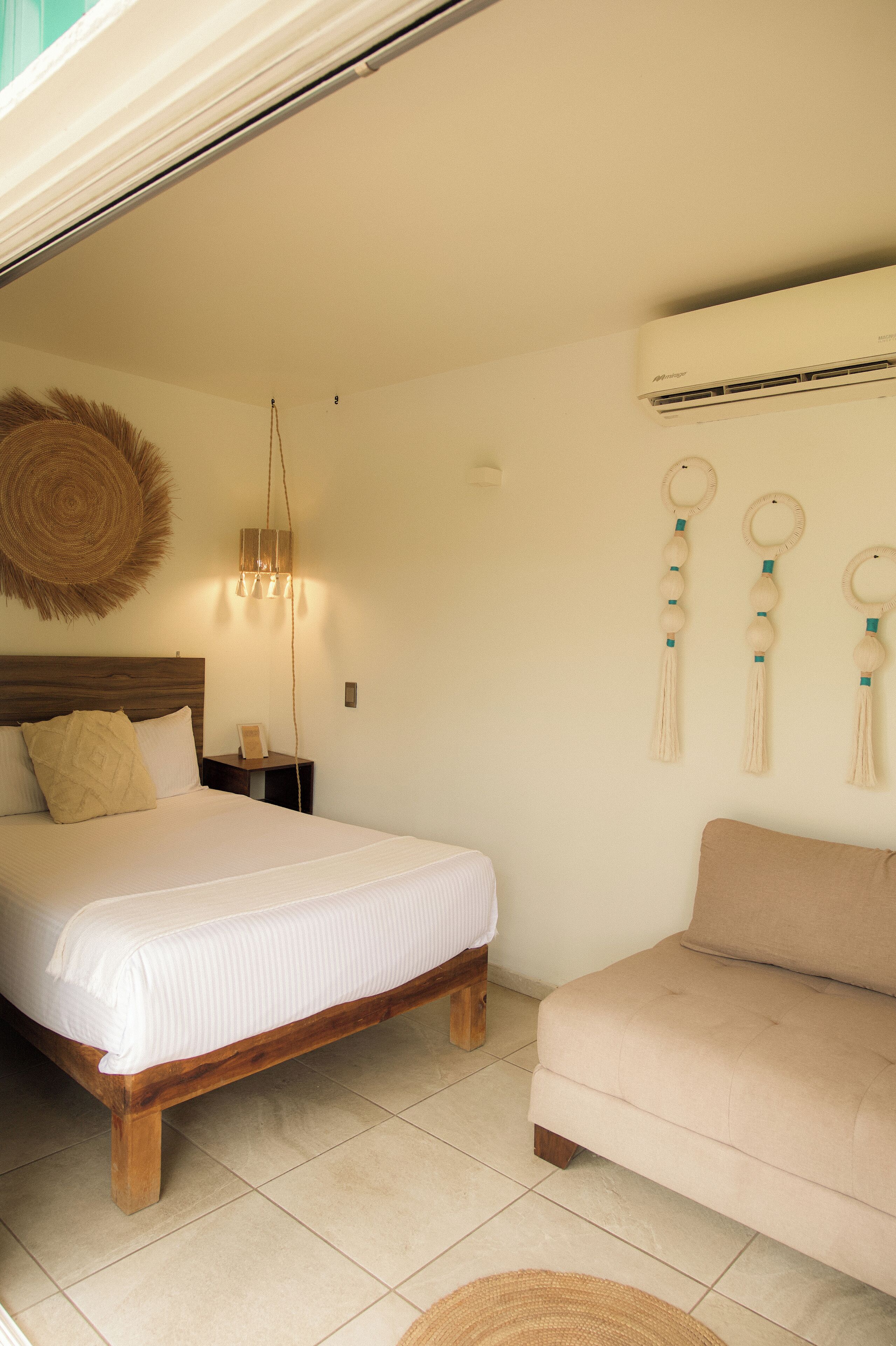 A bedroom with a bed, a nightstand, a wall-mounted air conditioner, and a sofa.