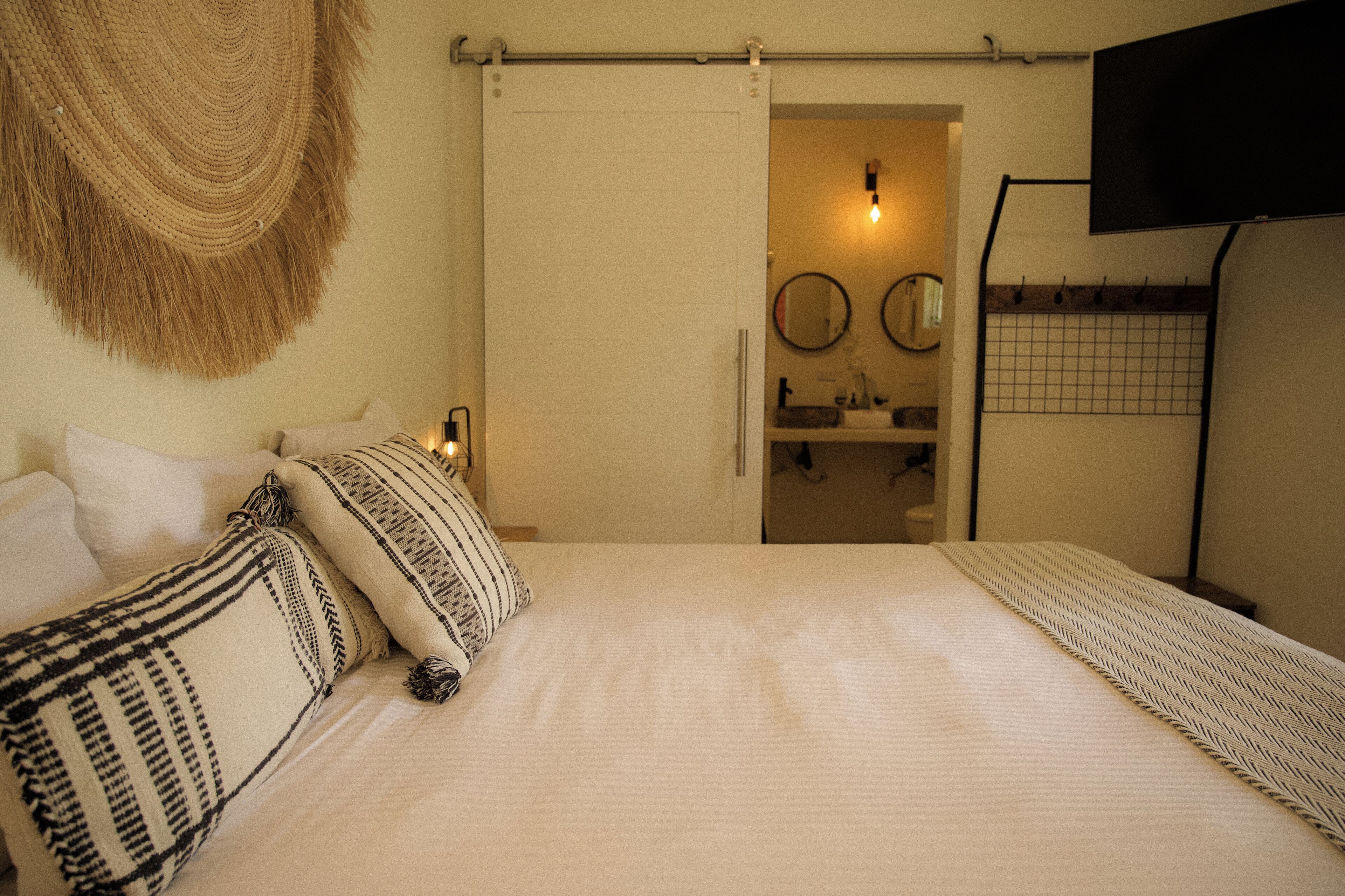 Ein Schlafzimmer mit Bett, Kissen, einem an der Wand montierten Fernseher und einer Tür zu einem Badezimmer.