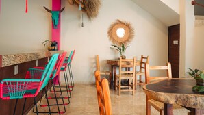 A dining area with a round wooden table, wooden chairs, and a colorful woven bench. - Nuiya Hoteles (Sayulita)