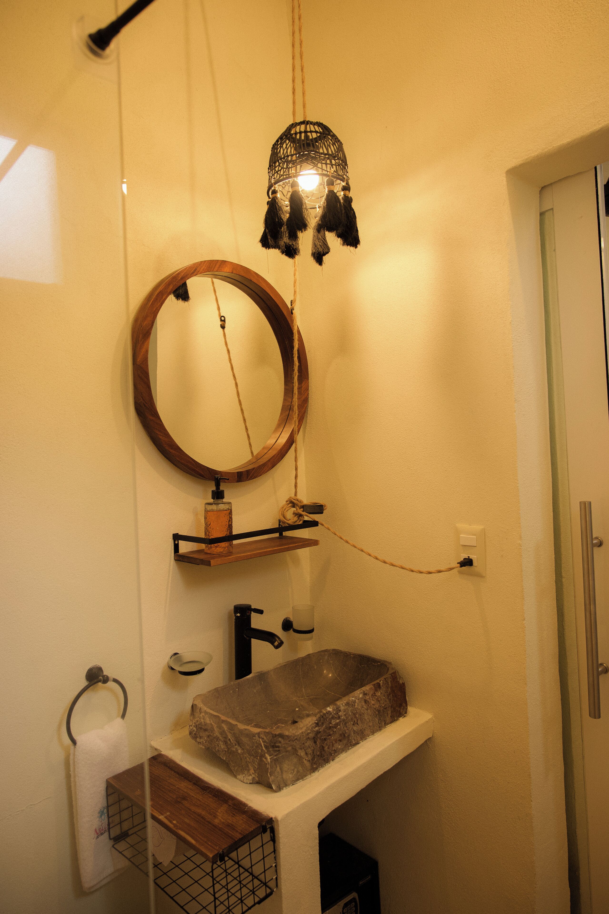 Een badkamer met een houten wastafelmeubel, een stenen wastafel, een ronde spiegel en een hangende lamp.