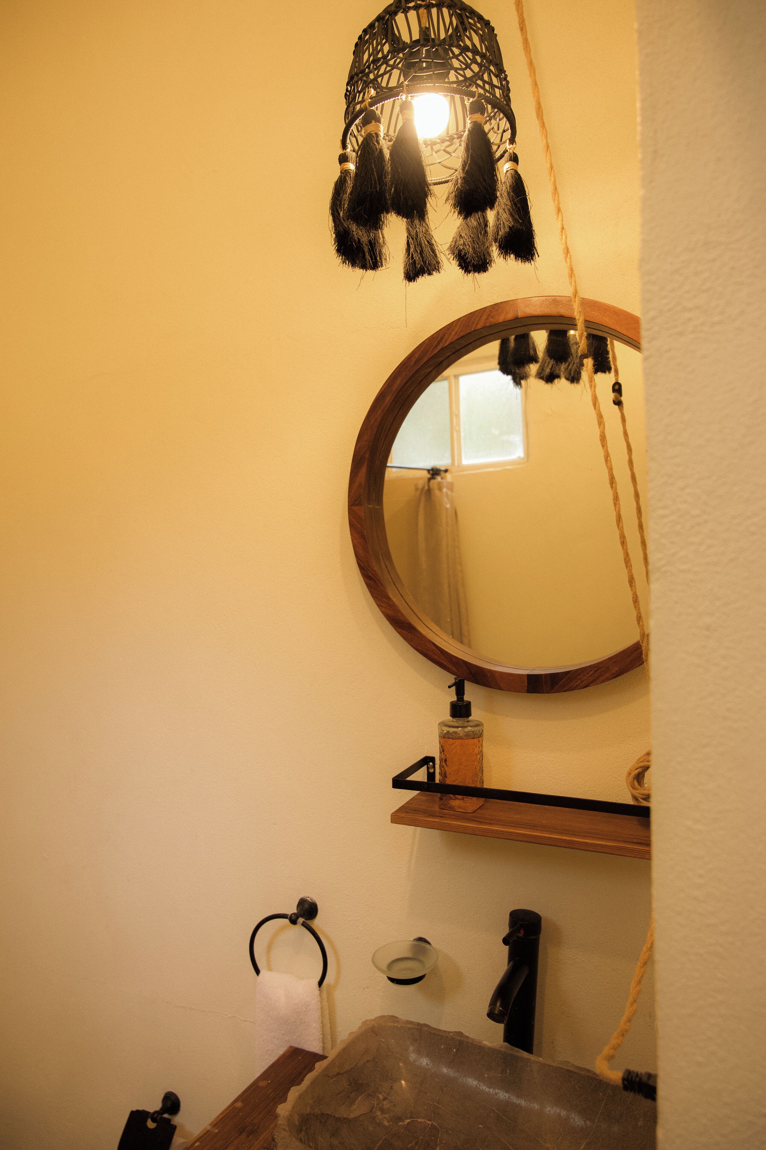 A bathroom with a wooden sink, a round mirror, a hanging light fixture, and a towel rack.