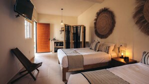 A bedroom with two beds, a TV mounted on the wall, a wooden wardrobe, and a bench. - Nuiya Hoteles (Sayulita)