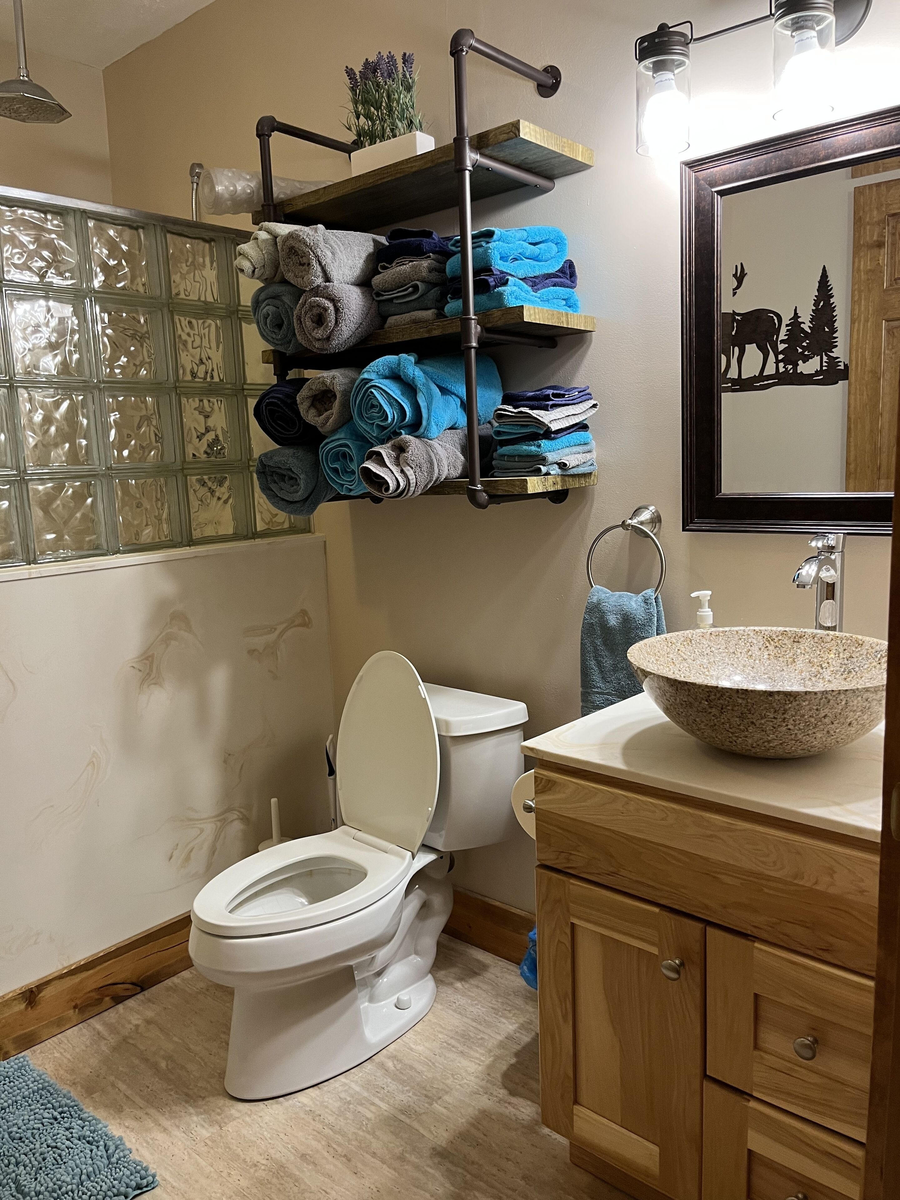 Une salle de bain comprenant des toilettes, un lavabo avec un receveur en pierre, un porte-serviettes avec des serviettes pliées et un miroir avec un cadre décoratif.