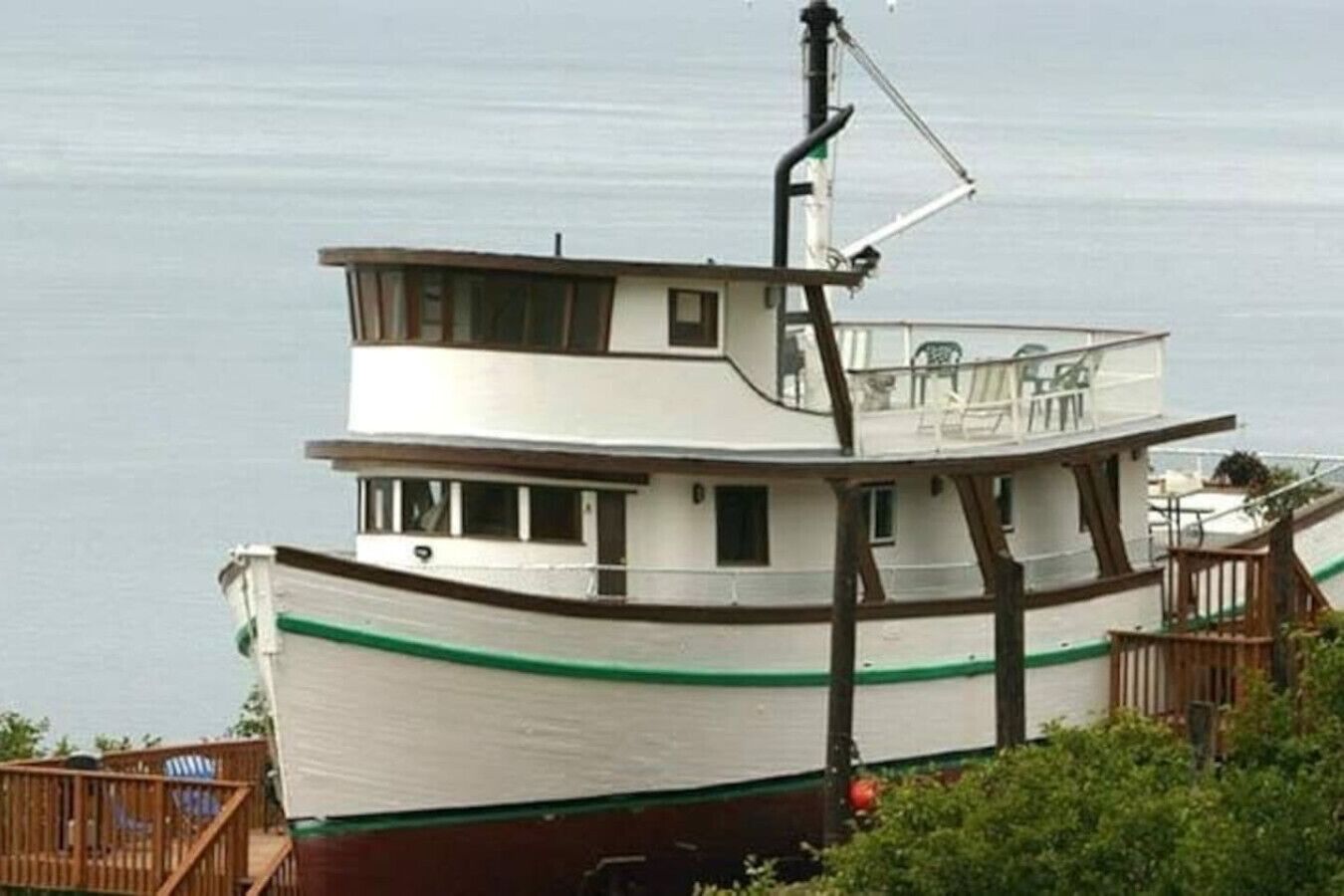 Un barco de varios pisos con estructura tipo cabina, una banda verde a lo largo del casco y una pequeña zona de cubierta con barandilla.