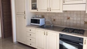 Cucina con mobili bianchi, forno a microonde, lavello e fornello.