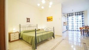 Una camera da letto con un letto a struttura in metallo, un comodino con una lampada, una coperta verde e un piccolo settimino in legno.