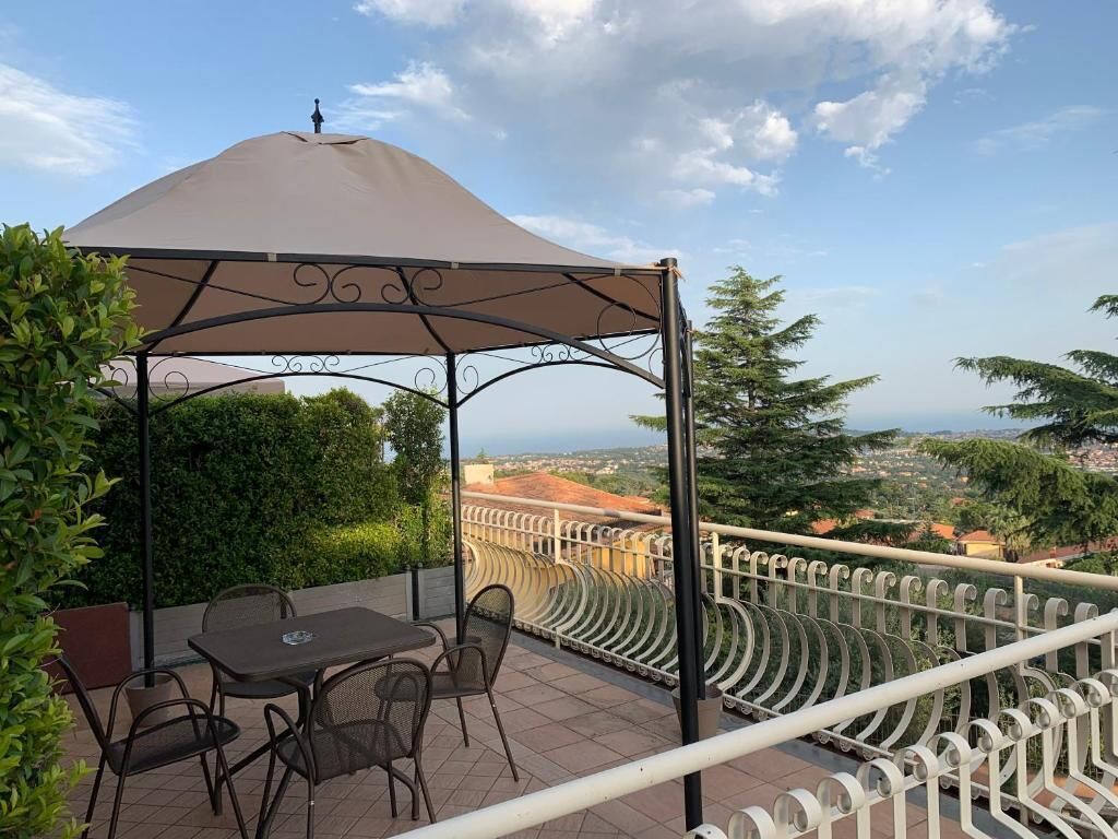 Een terras buiten met een tafel en stoelen, een pergola met een luifel, en een mooi uitzicht op het landschap.