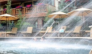 Un espace piscine avec des chaises longues et des parasols, une cascade et un mur en pierre.