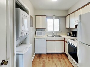 A compact kitchen with white appliances, a microwave, a sink, and a stove.