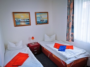 A hotel room with two beds, a nightstand, and two paintings on the wall.