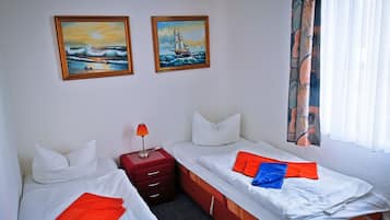 A hotel room with two beds, a nightstand, and two paintings on the wall.