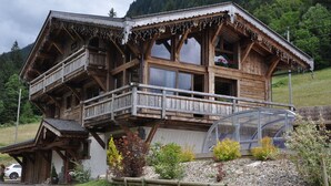 A wooden chalet with a balcony, a glass greenhouse, and a garden with various plants. - LUXURY CHALET IN MORZINE WITH POOL (Morzine)