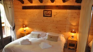 A wooden cabin bedroom with a large bed, two bedside tables with lamps, and a framed picture on the wall. - LUXURY CHALET IN MORZINE WITH POOL (Morzine)