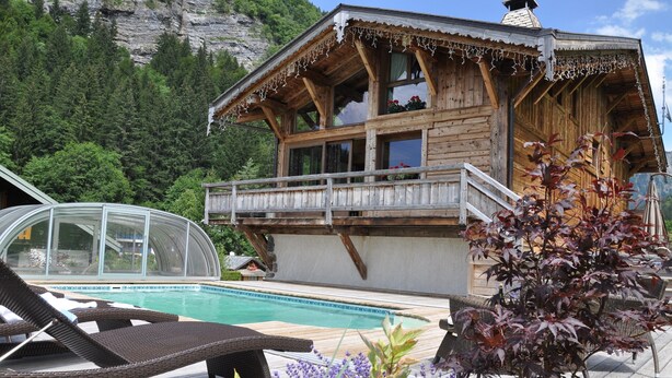 A wooden chalet with a pool, surrounded by greenery and mountains. - LUXURY CHALET IN MORZINE WITH POOL (Morzine)