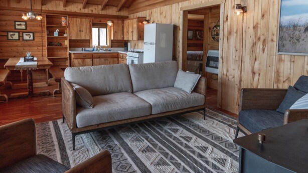 A log cabin interior with a wooden ceiling, a sofa, a dining table, and a kitchen area. - Zero Technology and100% Nature (Lake City)