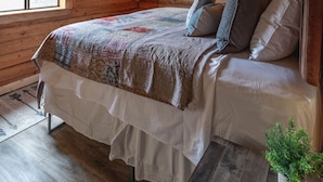 A wooden cabin bedroom with a bed, two windows, a wall-mounted lamp, and a small potted plant. - Zero Technology and100% Nature (Lake City)