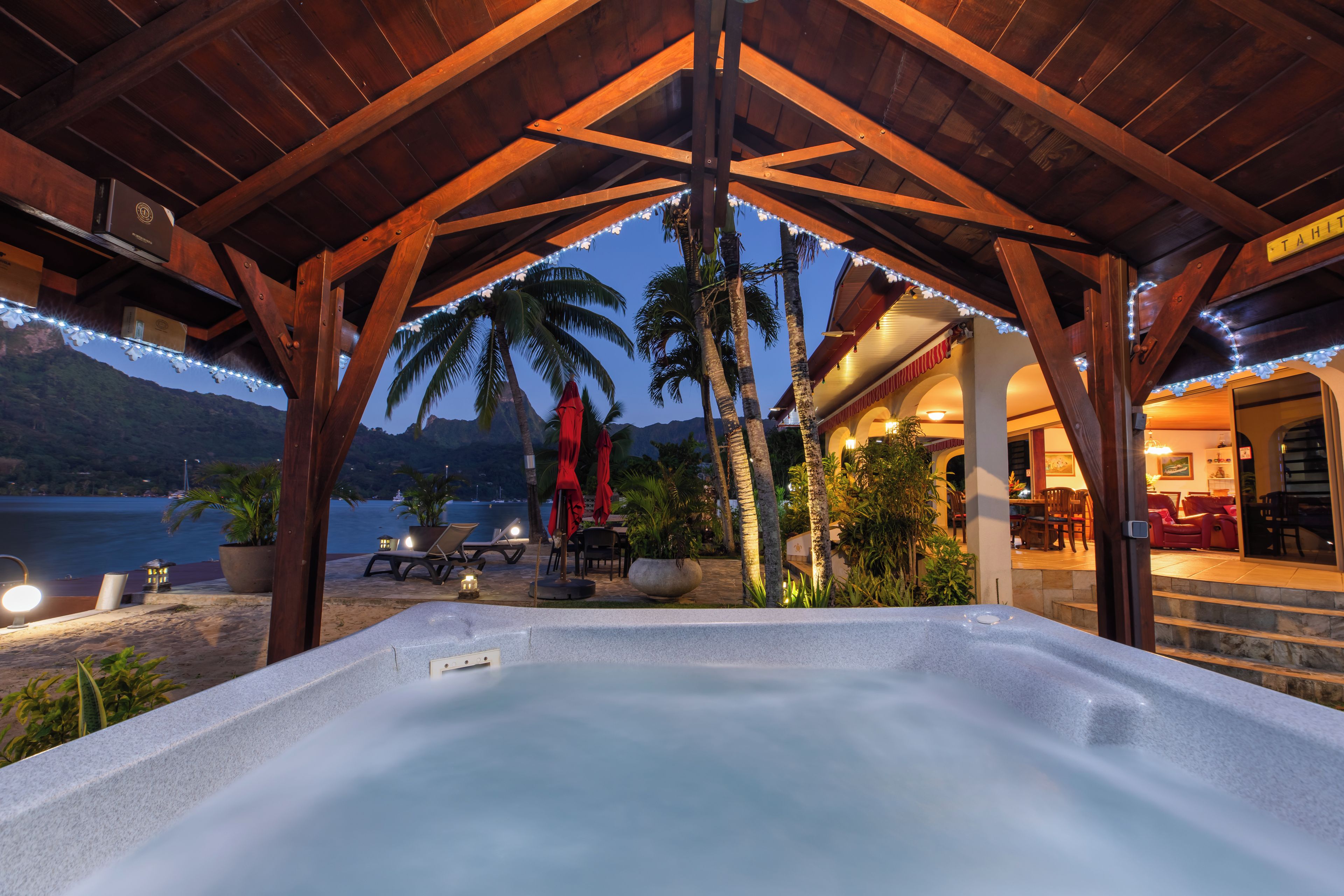 A hot tub area with a view of the sea and mountains, wooden beams, and string lights.