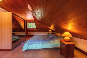Et soveværelse med skrå vægge, en seng med blomstret sengetøj, et natbord med en lampe og en skydedør til et andet rum.