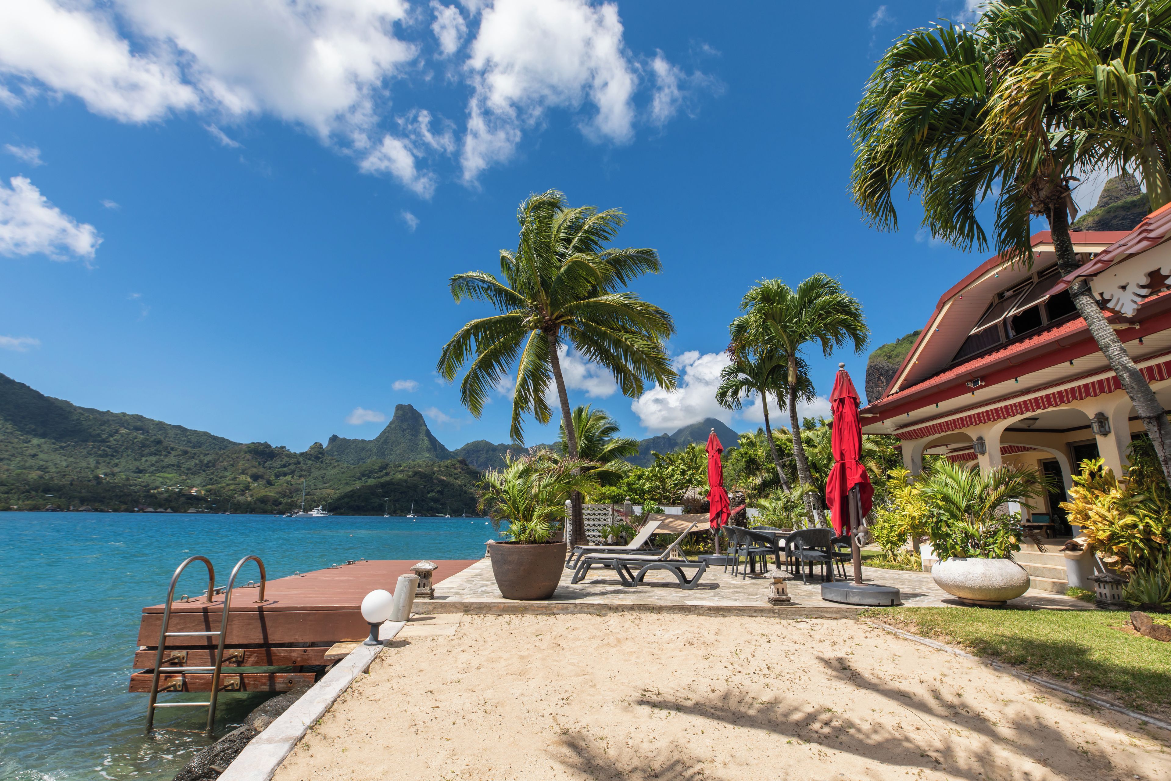 A beachside resort with a pool, lounge chairs, and a view of the ocean and mountains.