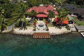 A beachfront property with a red-roofed building, a wooden dock, and clear turquoise water.