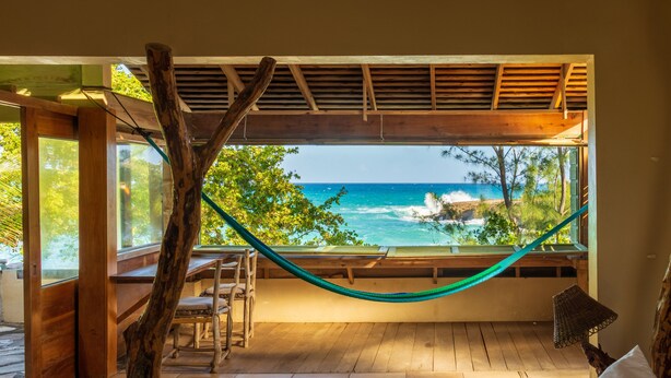 Een houten terras met een hangmat, een houten tafel en uitzicht op de oceaan.