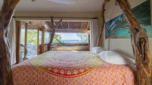 Een bed met een geborduurde spreideken, een hangmat en uitzicht op de oceaan door een raam.