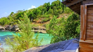 Een houten hutje met uitzicht op turquoise water en groene begroeiing.